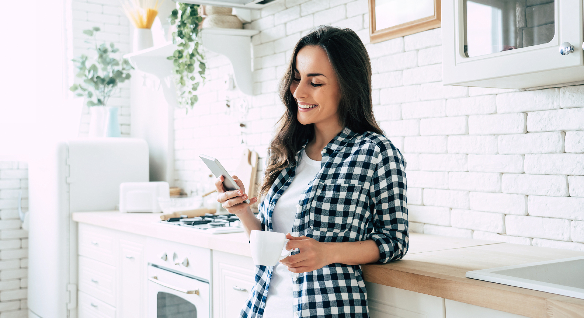Woman holding coffee cup and looking at her phone in kitchen